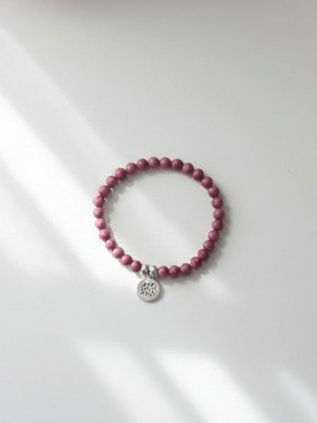 Pink beaded bracelet with a silver charm on a white background