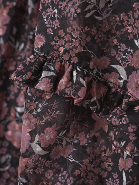 Detail of the fabric for Little girls A-line silhouette party dress. Black floral print. Small ruffled hem. The brand is Creamie.