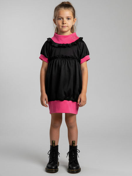 Young girl wearing a black and pink dress with black boots on a gray background