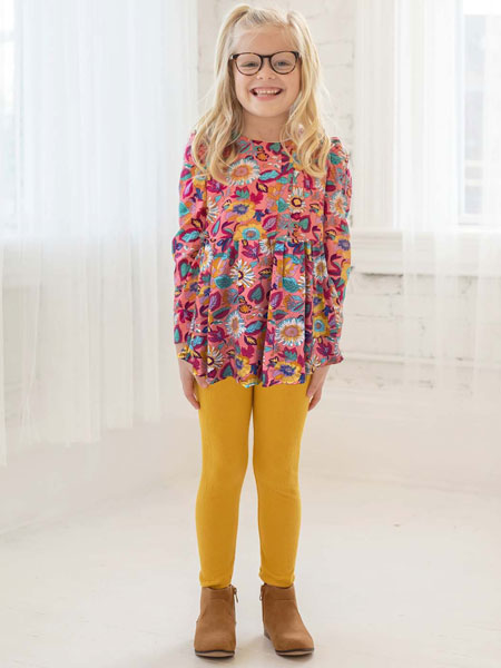 A girl wearing a colorful floral knit tunic top and mustard yellow leggings.