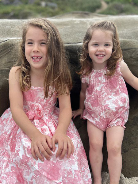 Girl modeling pink roses print dress with toddler girls in the matching toddler and baby girls romper.