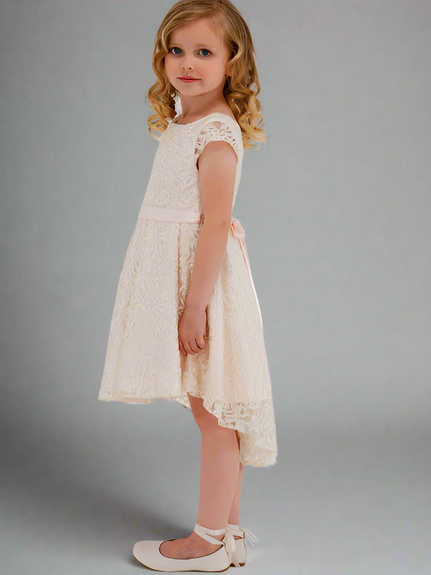 Young girl in a white and pale pink lace dress standing next to a large flower on a white background