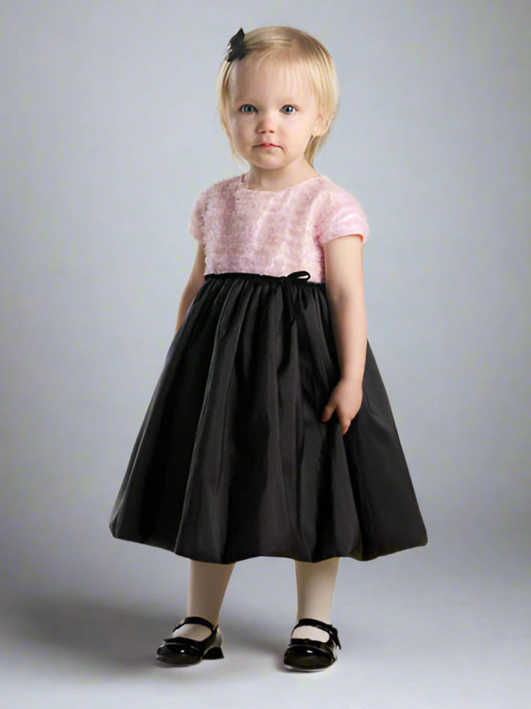 Young girl wearing a black dress with a pink top on a plain background