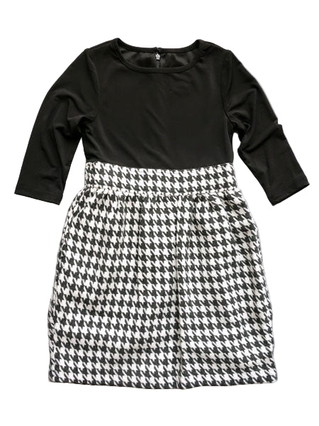 A black and white houndstooth girls dress with three quarter sleeves and a zipper closure at the back. The dress features a one-piece design with a black top and a black and white houndstooth skirt.