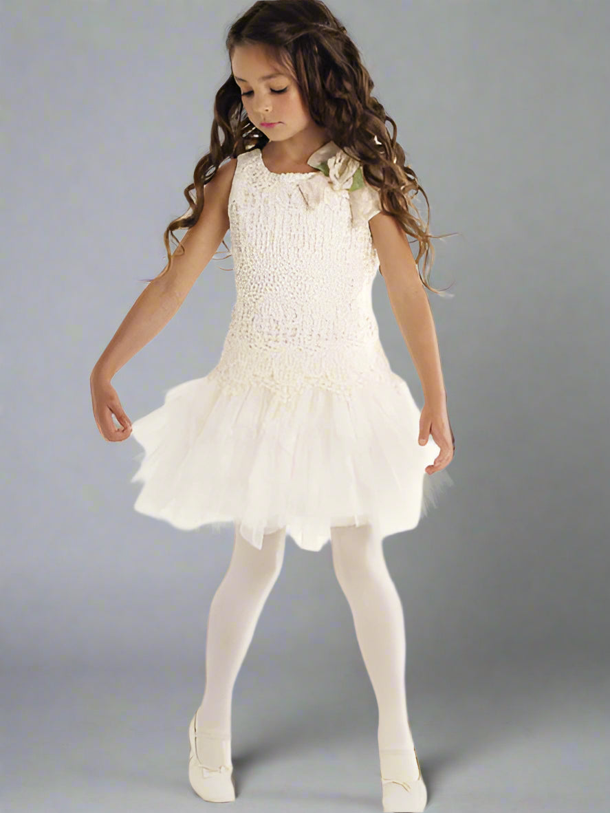 Young girl wearing an ivory dress with a floral bow on a gray background