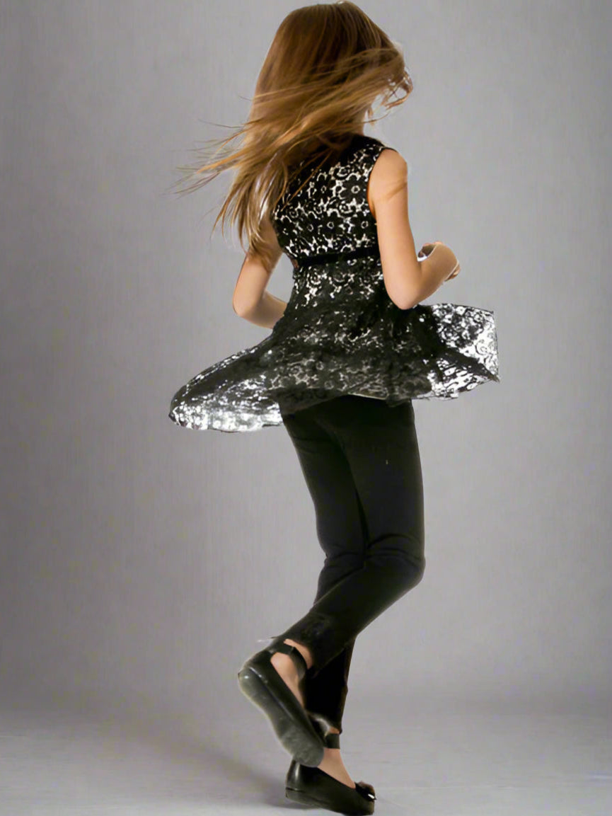 Girl wearing a black lace tunic  top and black leggings against a gray background.
