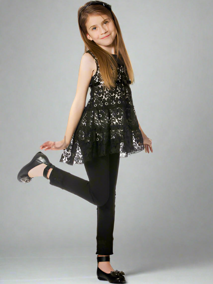 Young girl wearing a black lace top and black pants on a gray background.