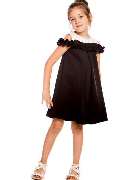 Girls black party dress, cold shoulder style. White accent fabric at neckline.