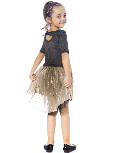 Girls posing back view of   high low party dress. Black metallic knit top with gold chiffon skirt over black tulle. Skirt is scattered with small silver squares. Round scoop neck with back bow across shoulders.