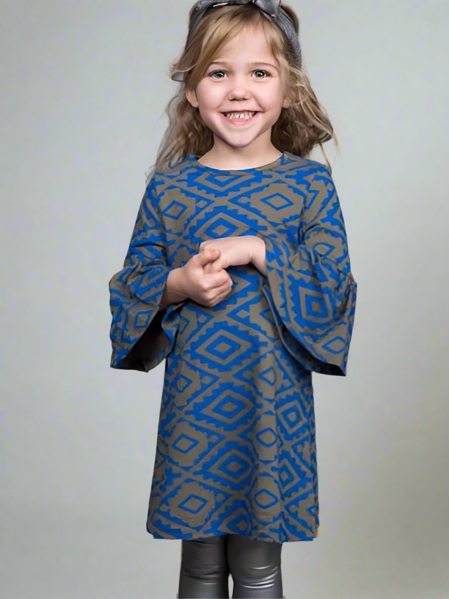 Young girl wearing a blue and olive green patterned dress against a plain background