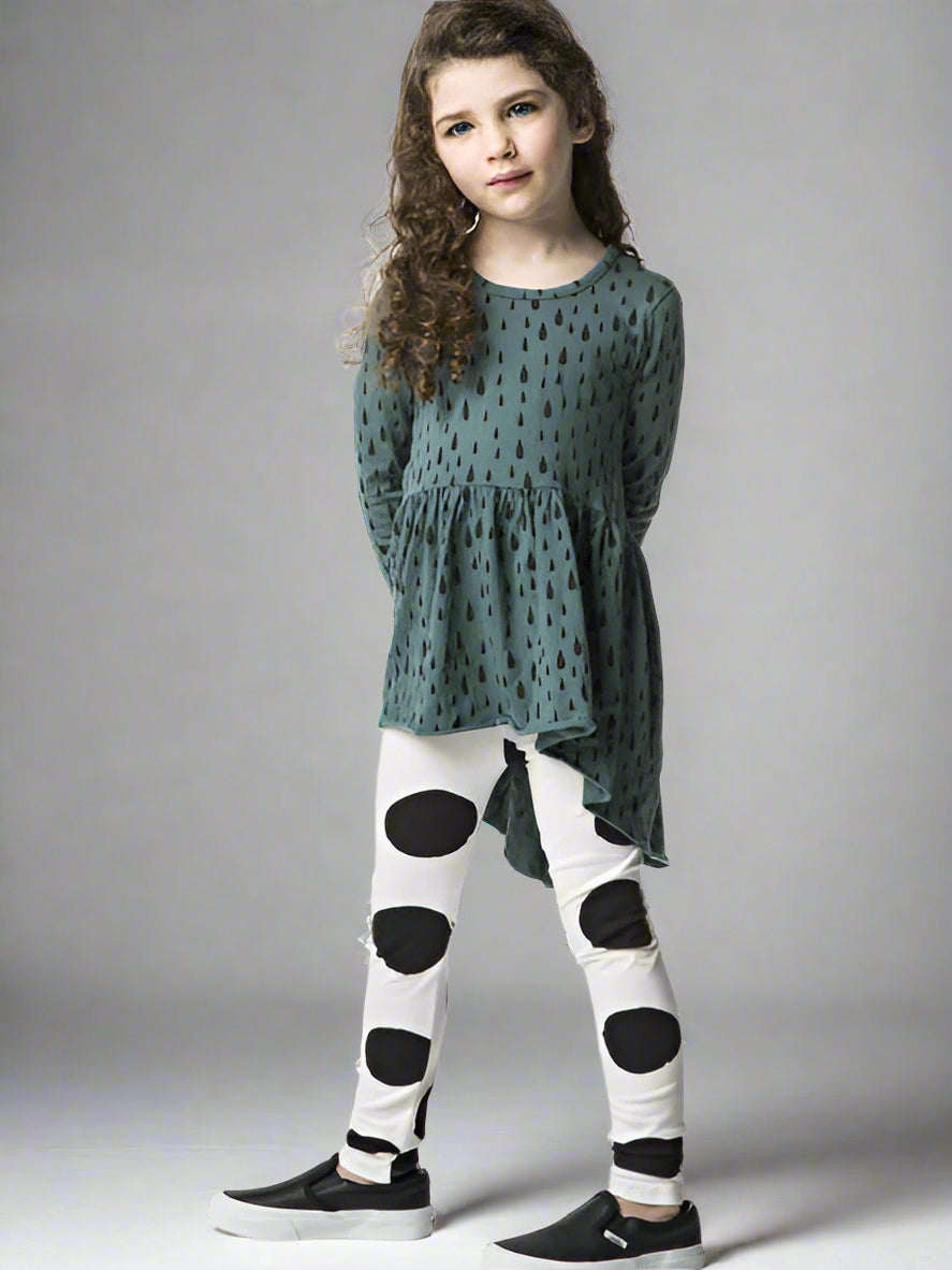 Young girl wearing a teal and black patterned top and black and white polka dot leggings.