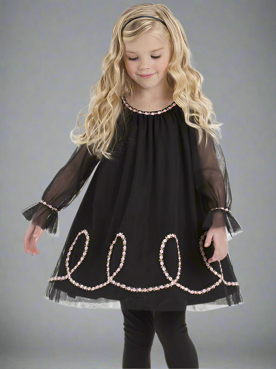 Young girl wearing a black dress with decorative trim on a white background