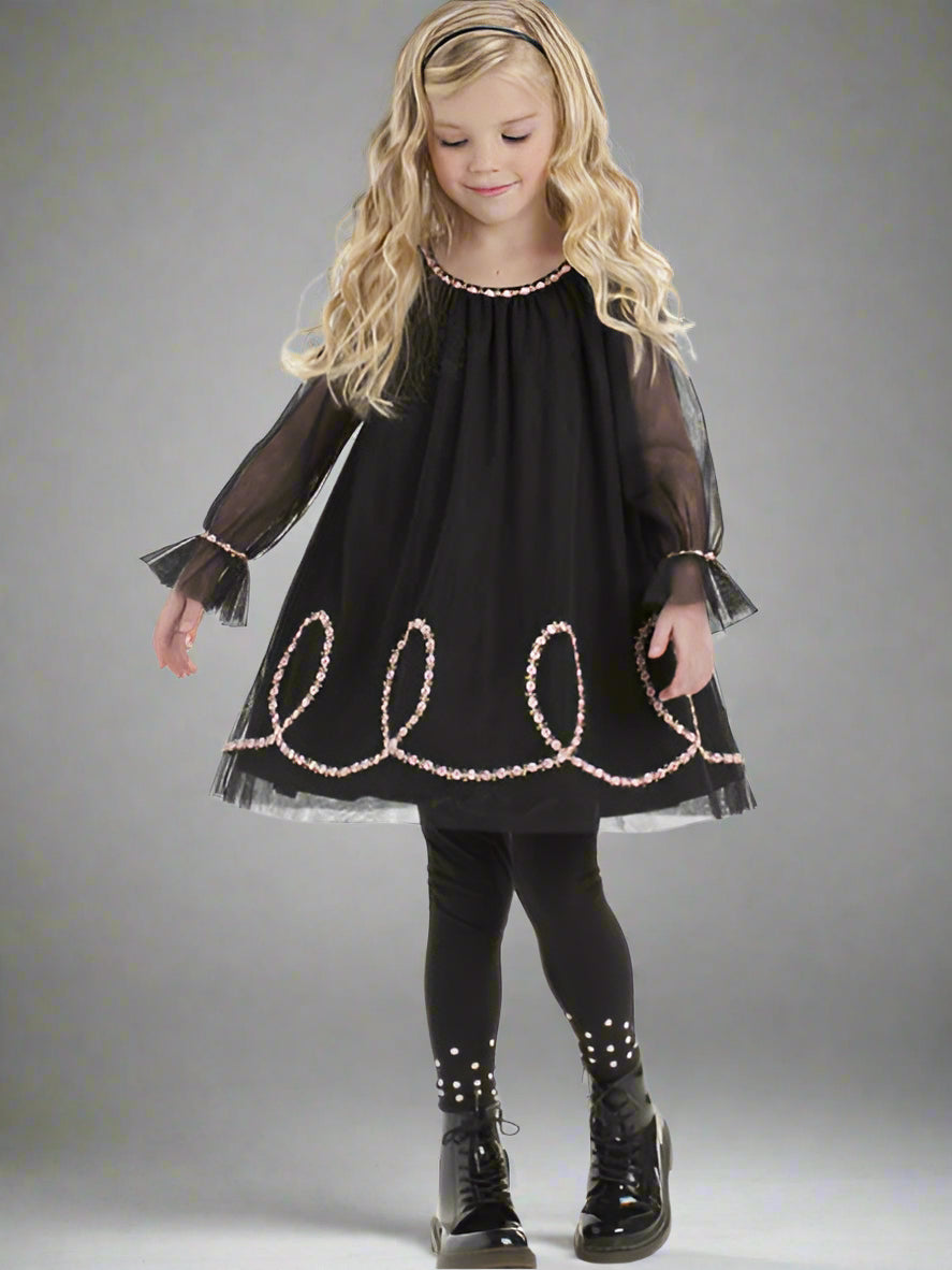 Young girl wearing a black dress with decorative trim on a gray background