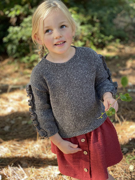 Little girl wearing rust skirt and gray sweater top. Gathered elastic waist. Front faux center plaquette with brown button at center.