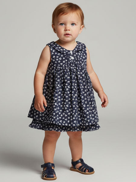 Baby wearing a navy floral dress on a plain background
