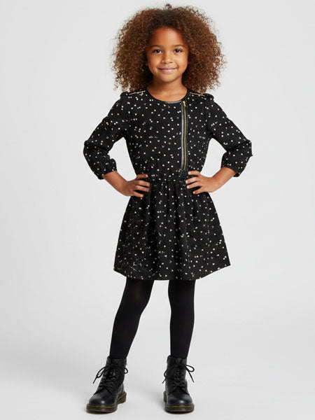 Young girl wearing a black dress with white patterns and black boots on a light gray background