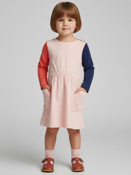 Child wearing a pink dress with red and blue sleeves on a plain background
