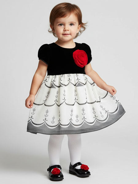 Child wearing a black top with a red flower and a white dress with black patterns on a white background