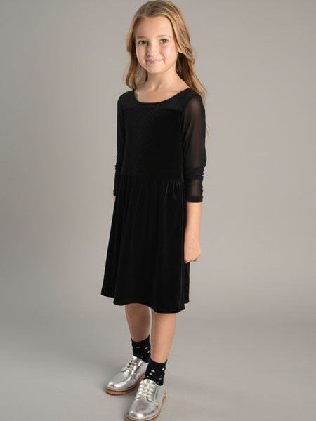 Young girl wearing a black dress with sheer sleeves against a gray background