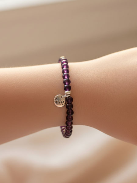 Purple beaded bracelet with a silver charm on a wrist against a beige background