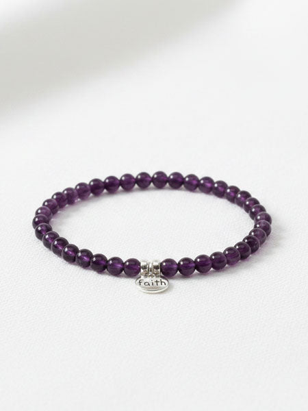 Purple beaded bracelet with a 'faith' charm on a white background