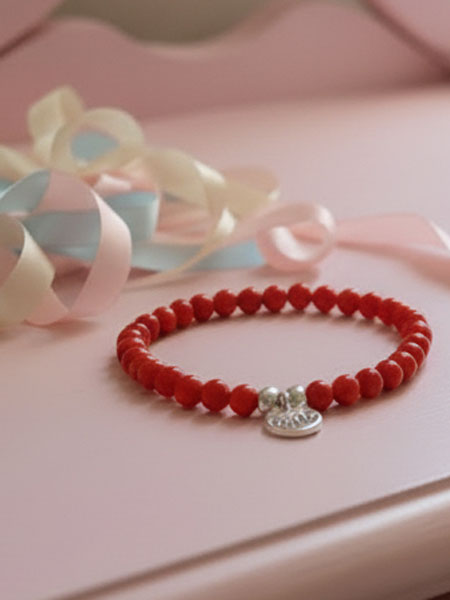 Red beaded bracelet with a silver charm on a pink surface