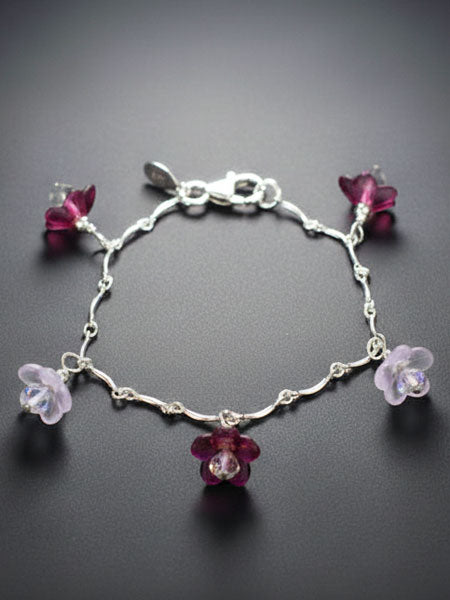 Silver bracelet with purple flower charms on a dark background
