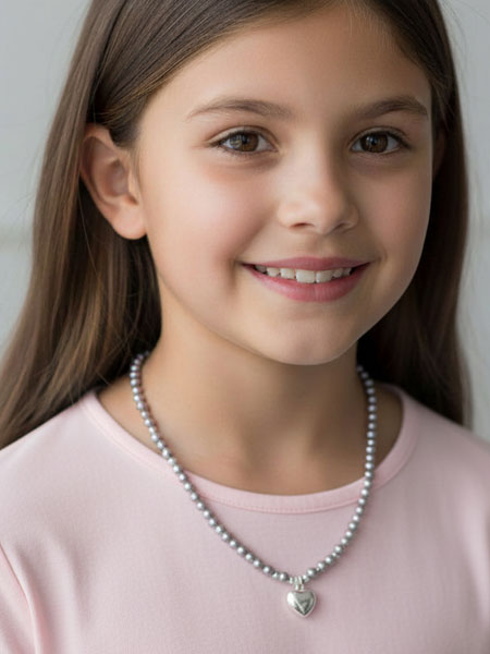 Young girl wearing a pearl necklace with a heart pendant against a plain background