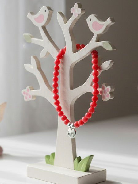 Red beaded bracelet with a silver charm on a decorative tree stand with bird designs.