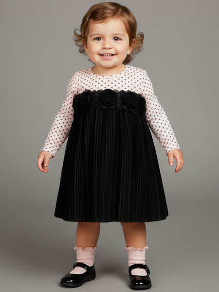 Child wearing a black dress with a white polka dot shirt on a gray background
