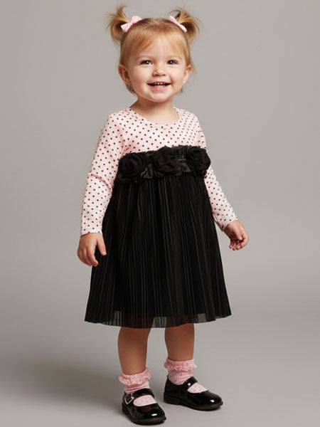 Child wearing a pink polka dot top and black pleated skirt  dress with a pink  hair bow on a gray background