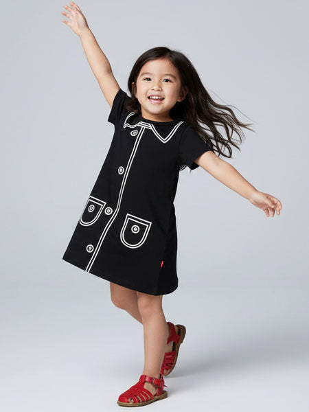 Child wearing a black dress with white buttons on a gray background
