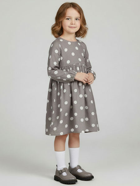Young girl wearing a gray dress with white polka dots on a plain background