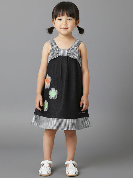 Young girl wearing a black dress with floral patterns and a checkered bow on a gray background