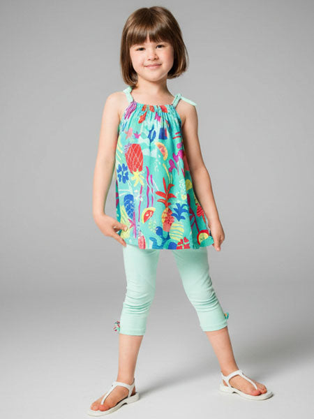 Young girl wearing a colorful floral top and light green pants on a gray background