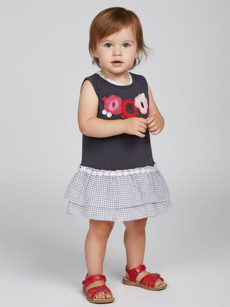 Child wearing a black sleeveless top with red and white designs and a white skirt with black patterns on a light gray background.