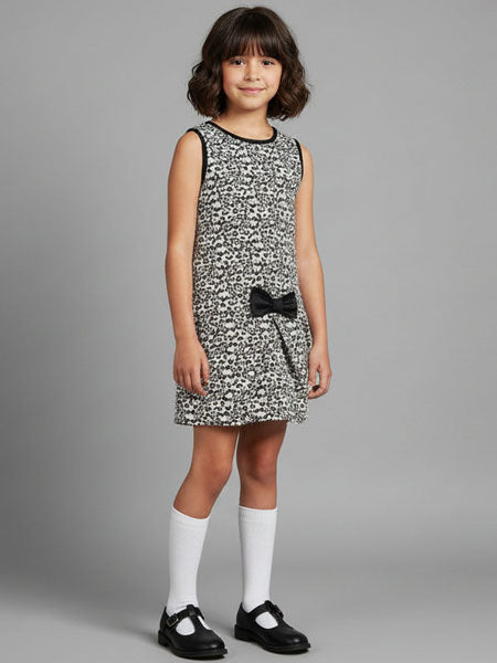 Young girl wearing a patterned dress with a black bag over her shoulder against a gray background