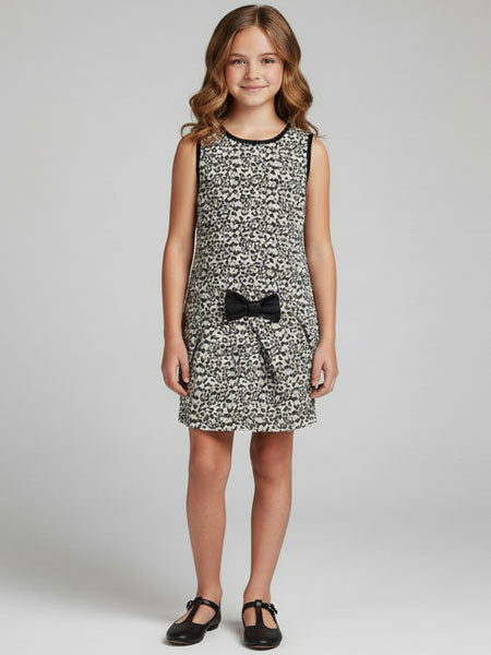 Young girl wearing an animal print patterned dress with a black bow on a plain background