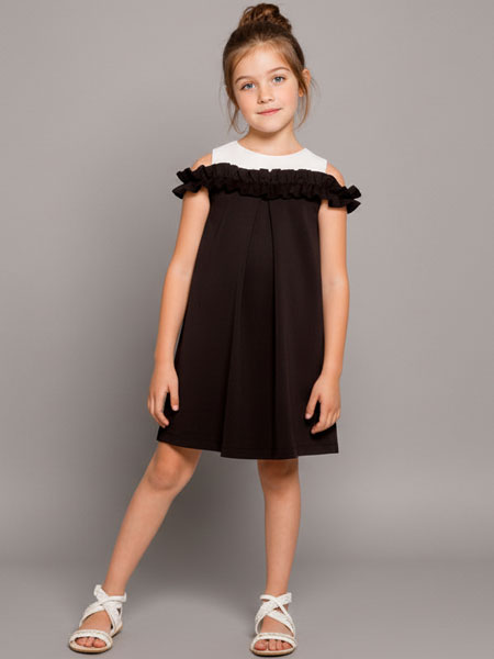Young girl wearing a black dress with white ruffled details on a gray background