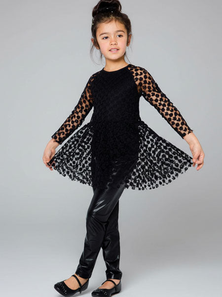 Young girl wearing a black outfit with dot print sleeves and skirt against a gray background