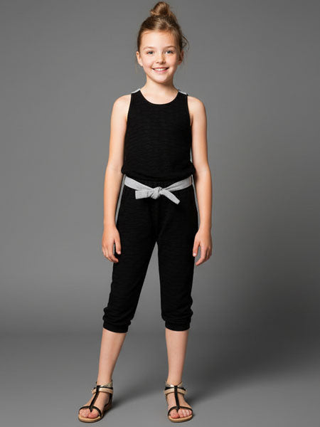 Young girl wearing a black jumpsuit, capri length with a gray belt on a gray background