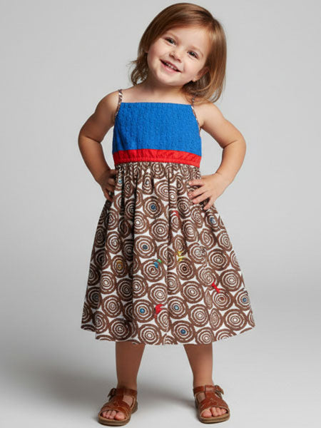 Child wearing a blue top and brown patterned skirt with red trim on a plain background