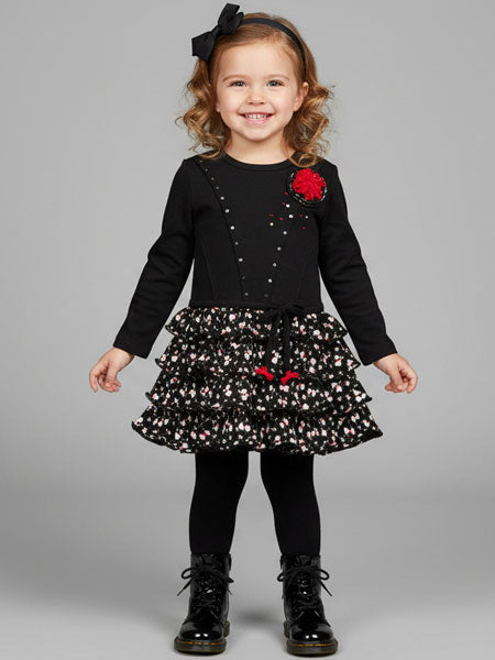 Child wearing a black dress with red flowers and floral skirt on a gray background