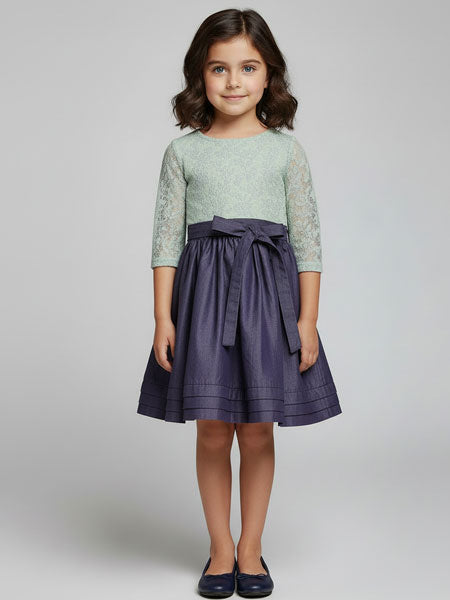 Young girl wearing a green top and purple skirt on a plain background