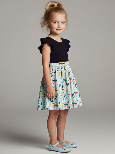 Young girl wearing a black top and colorful skirt against a gray background