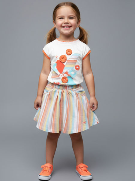 Young girl wearing a colorful outfit with a striped skirt and orange shoes on a gray background