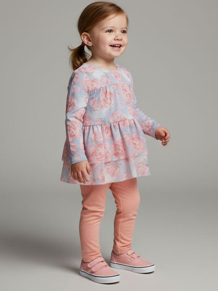 Young girl wearing a floral dress and pink leggings on a gray background