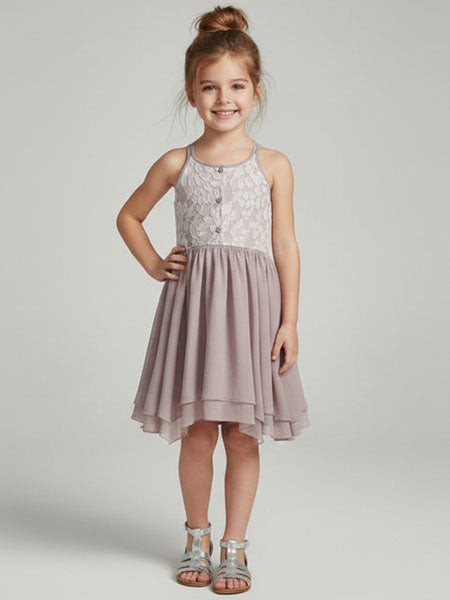 Young girl wearing a taupe dress with a white lace top on a plain background