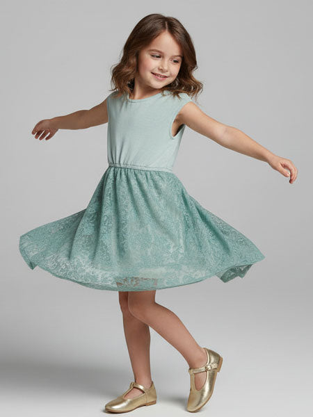 Young girl in a light blue dress with a subtle pattern, standing against a plain background.