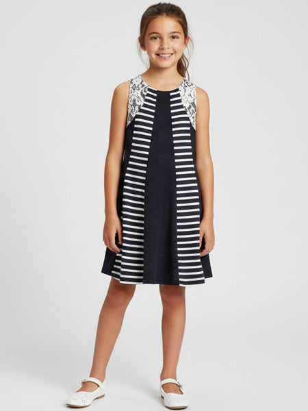 Young girl wearing a navy and white striped dress with floral lace details on a white background
